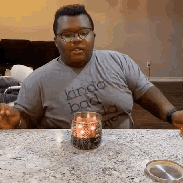 a man wearing a kinda bad shirt sits at a table with a candle in front of him