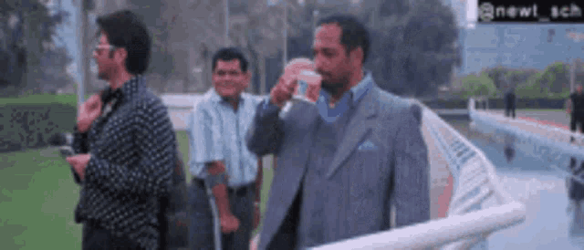 a man in a suit drinks from a cup while standing next to another man