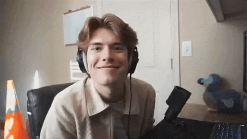 a young man wearing headphones is smiling while sitting in front of a microphone .