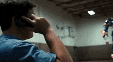 a man in a blue shirt is talking on a cell phone while a superhero is flying in the background .