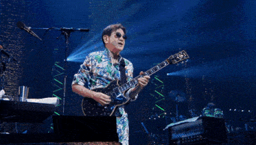 a man in a floral suit playing a guitar on stage