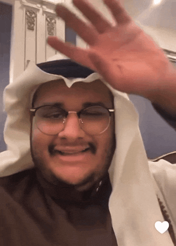 a man wearing glasses and a white scarf waves his hand