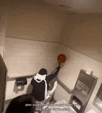 a man holding a basketball in a public restroom with a hand dryer