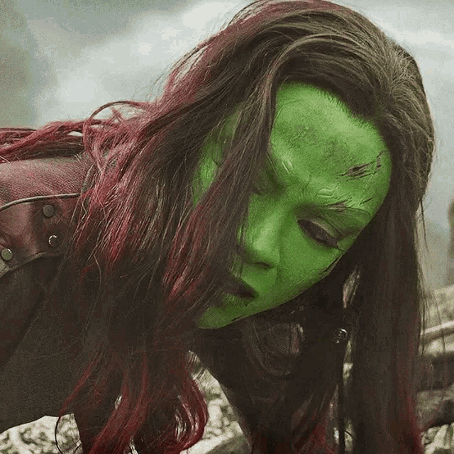 a woman with red hair and a green mask on her face .