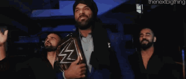a man in a suit is holding a wrestling championship belt while standing next to two other men .