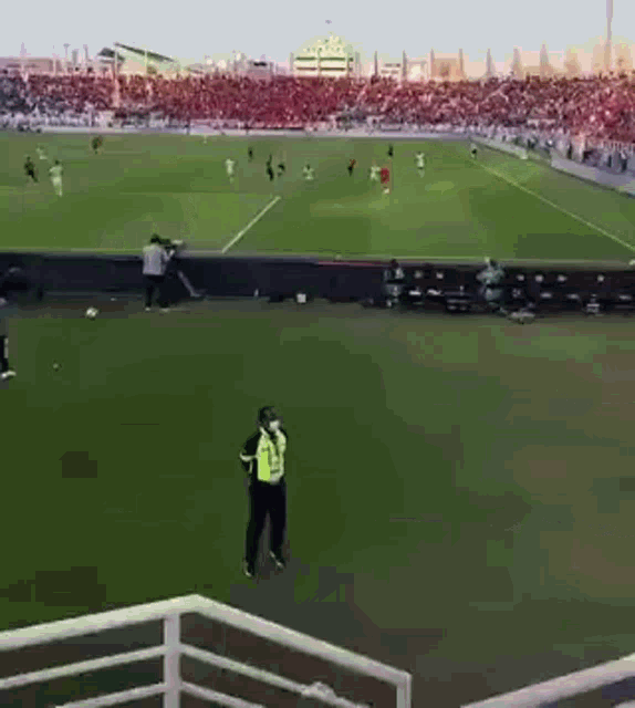 a man in a yellow vest stands on a soccer field watching a game