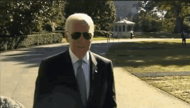 a man in a suit and tie wearing sunglasses is walking down a path