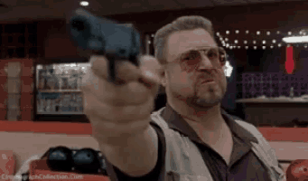 a man is pointing a gun at the camera while standing in a bowling alley .