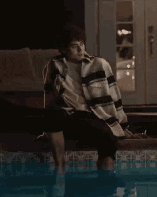 a man in a striped shirt sits next to a swimming pool