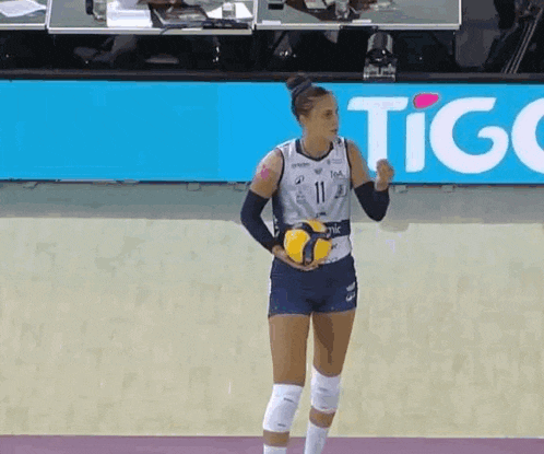 a female volleyball player is holding a ball in front of a sign that says tigo .