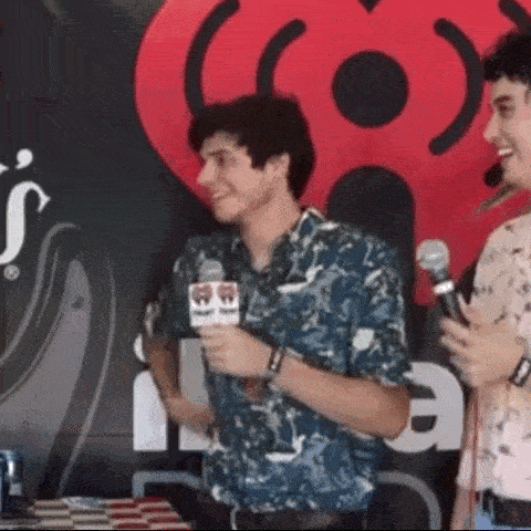 a man is talking into a microphone while another man looks on .