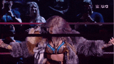 a woman in a fur coat is standing in a wrestling ring with us written on the bottom