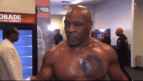 a man with a tattoo on his chest is standing in front of a gatorade cooler