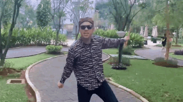 a man wearing sunglasses and a headband is dancing on a path in a park