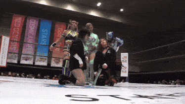 a group of women in a wrestling ring with neo genesis banners on the wall behind them