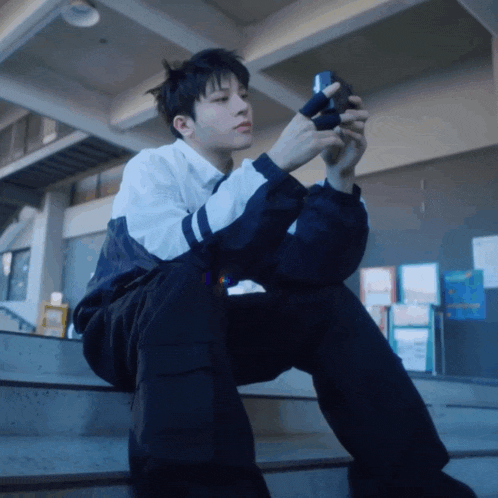 a young man sits on a set of stairs looking at his cell phone