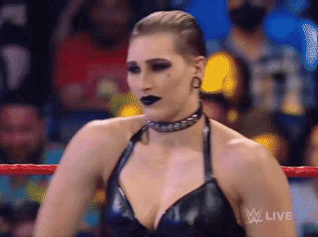 a woman is standing in a wrestling ring wearing a choker and a black dress .