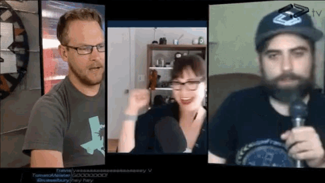 a man with glasses and a beard is talking into a microphone while a woman looks on