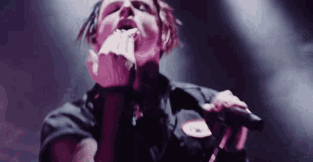a man is singing into a microphone on a stage while holding a piece of paper in his mouth .
