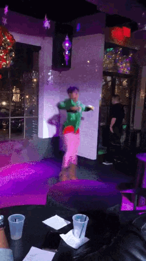 a man in a green sweater and pink pants is dancing on a stage