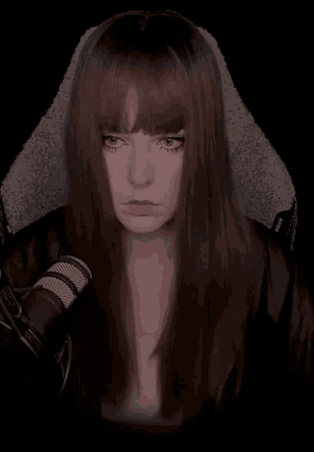 a woman with long brown hair is sitting in front of a microphone and looking at the camera