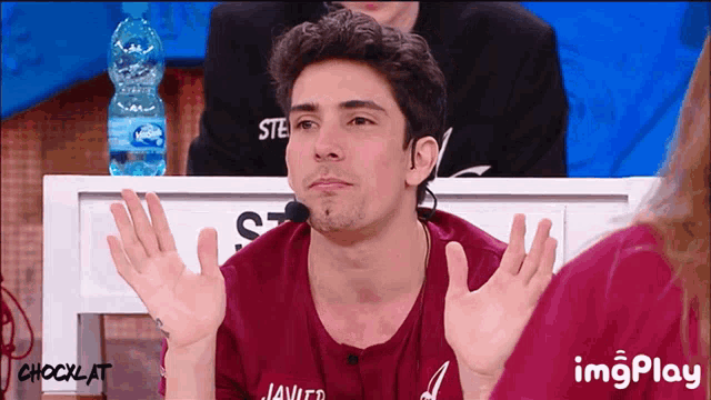 a man in a maroon shirt with the name javier on it is sitting at a table