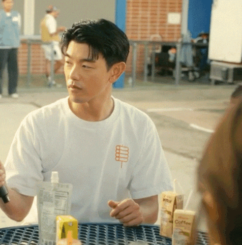 a man in a white shirt sits at a table with two cartons of coffee