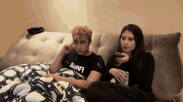 a man and a woman are sitting on a couch with the man wearing a black shirt that says ahava
