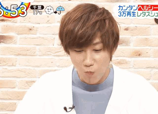 a man with a microphone on his neck is eating something in front of a brick wall
