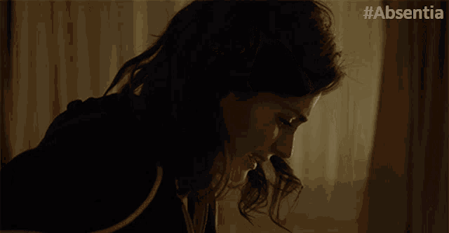 a woman adjusts her hair with the hashtag #absentia on the bottom