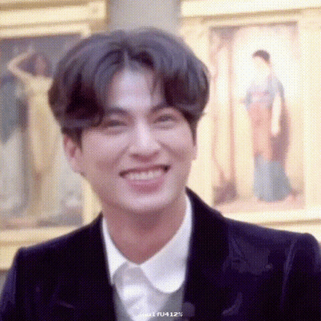 a man in a suit and white shirt is smiling in front of a wall of paintings .