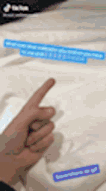 a person is pointing at a white shirt with a blue sticker that says ' supreme ' on it .