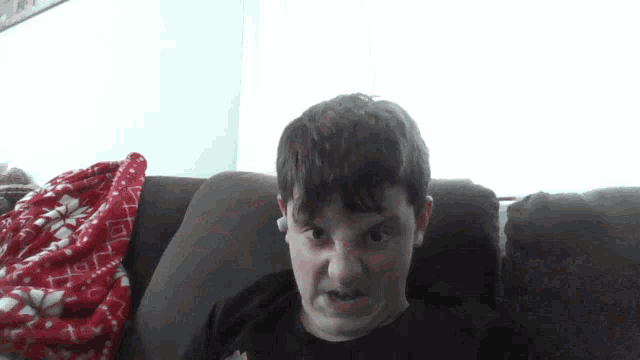 a young boy is sitting on a couch with a red blanket on the couch