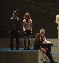 a group of people are standing and sitting on a stage in a dark room