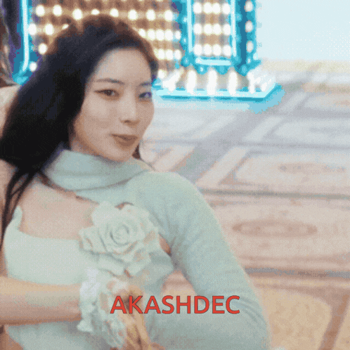 a woman in a white dress with a flower on her chest is standing in front of a sign that says " akashdec "