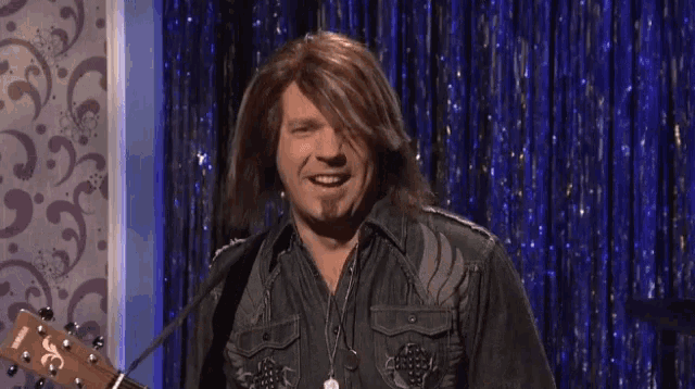 a man in a wig is holding a guitar with the letter s on it