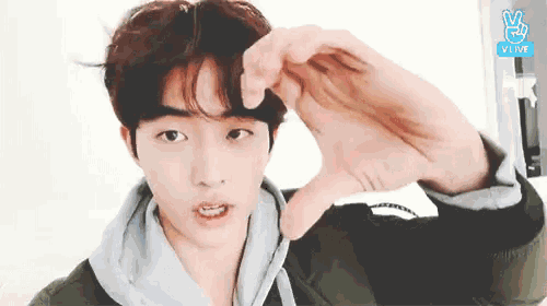 a young man is making a heart shape with his hands while looking at the camera .