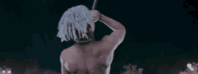 a man with white dreadlocks is standing in the dark without a shirt .