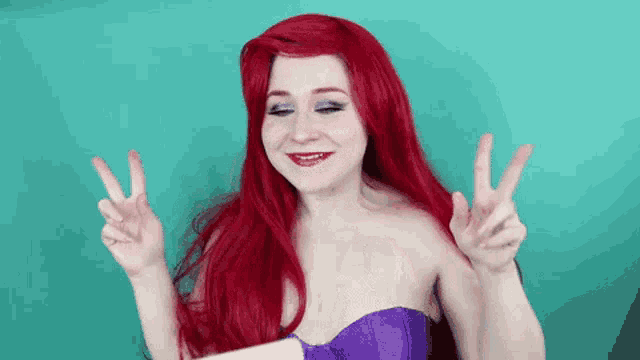 a woman with red hair and a purple dress is giving a peace sign .
