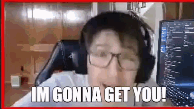 a man wearing headphones and glasses is sitting in front of a computer screen and saying `` im gonna get you ! ''