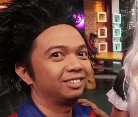 a man wearing a wig is smiling in front of a chalkboard that says stock