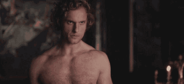a shirtless man in a dark room looks at the camera