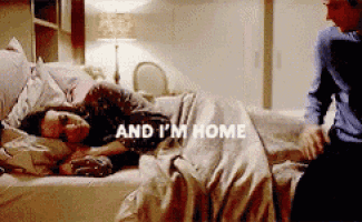 a man is sitting next to a woman laying on a bed with the words " and i 'm home " written on it