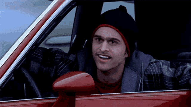 a man wearing a beanie and a plaid shirt is sitting in a red car