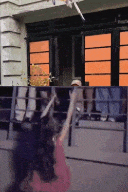 a woman in a pink dress is standing in front of a building with orange windows