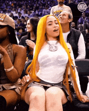 a woman with long orange hair is sitting in the stands at a basketball game wearing a number 12 hat