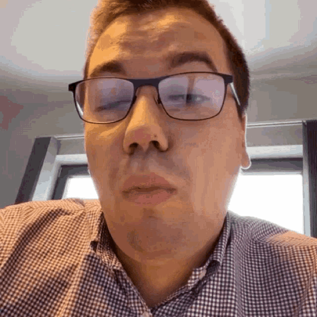 a man wearing glasses and a plaid shirt is making a face