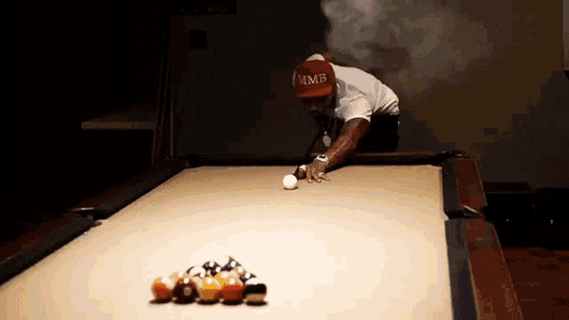 a man wearing a red hat that says mmb playing pool