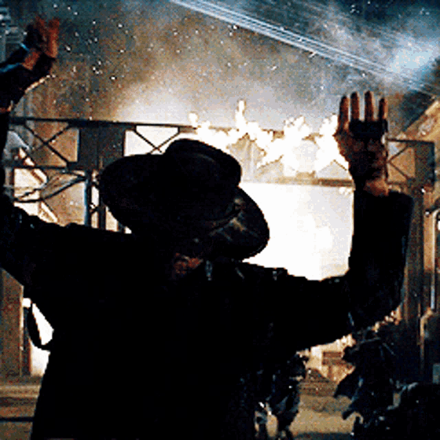 a man in a black hat is standing in front of a burning building