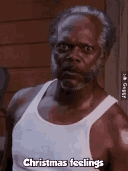a man with a beard is wearing a white tank top and saying `` christmas feelings '' .